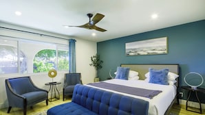 A modern bedroom with a large bed, a blue sofa, a small table, and a ceiling fan. - The Clubhouse: Sleep 20+, Pool, Pickleball, Hot Tub, Outdoor Movie, Arcades (Indio)