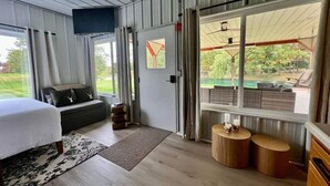 Een slaapkamer met een bed, een bank, een klein tafeltje en uitzicht op een zwembad door een glazen deur.