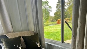 Een kamer met een bank, een klein houten bijzettafeltje en uitzicht op een tuin door een raam.