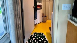 Een gang met een gele vloer, een witte deur en een vloerkleed met de tekst 'YOU LOOK GOOD'.