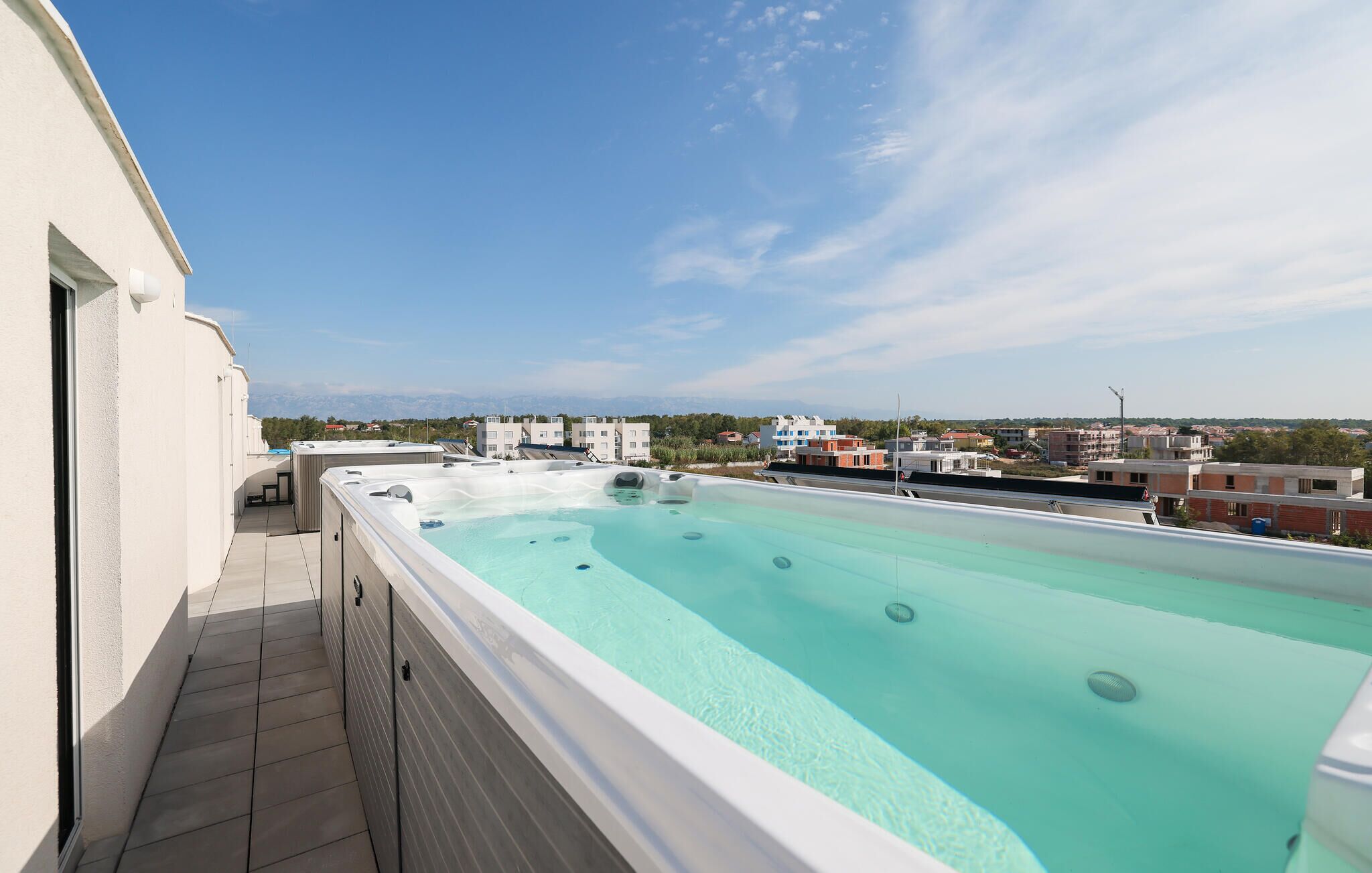Una piscina sul tetto con acqua cristallina, circondata da un edificio bianco e con vista su uno skyline urbano.