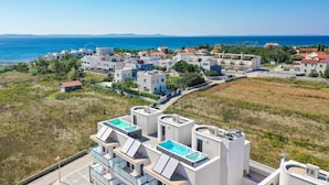 A coastal residential area with modern buildings, a swimming pool, and a view of the sea.