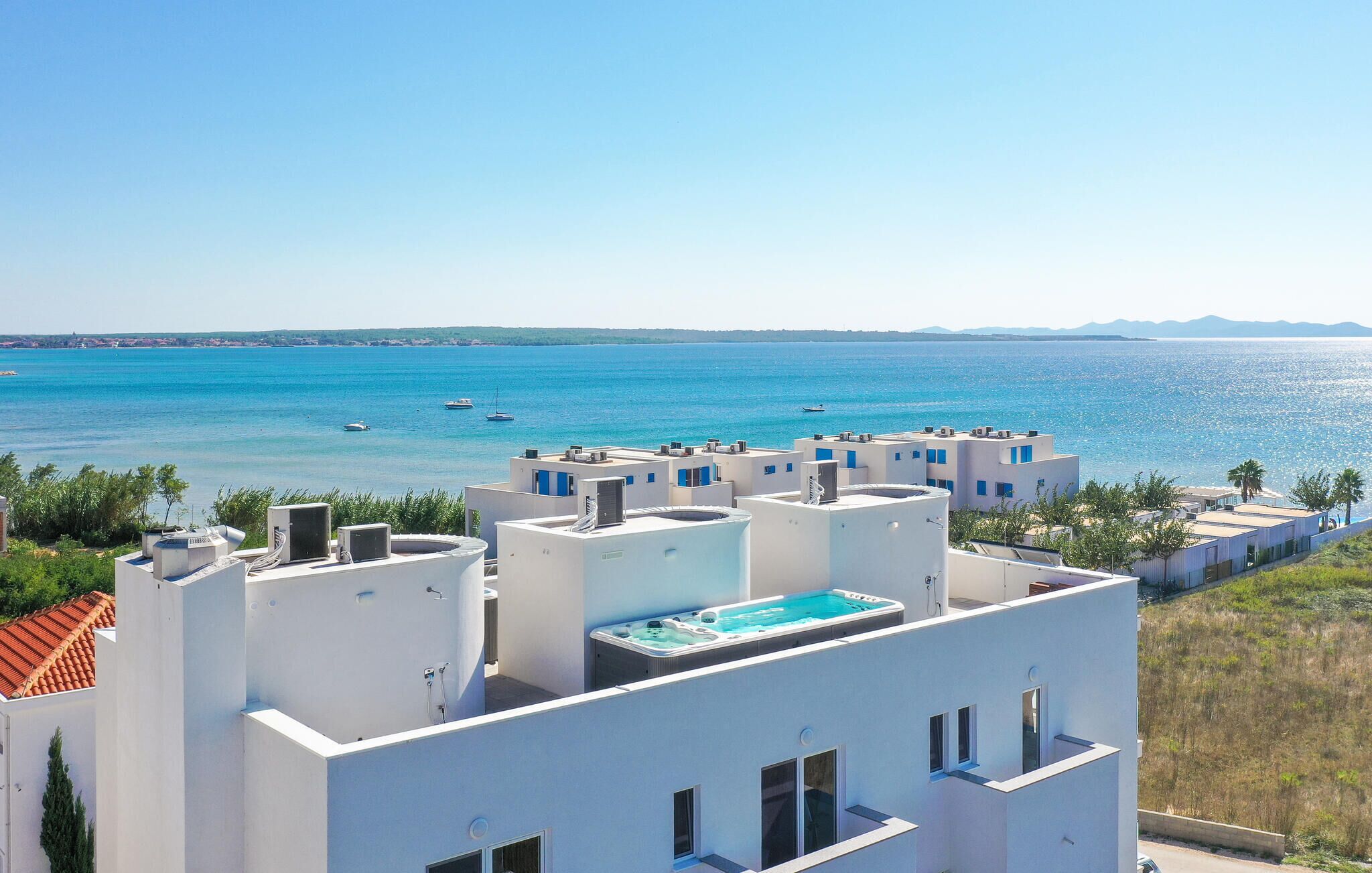 Un edificio costero con piscina en la azotea, paredes blancas y vistas despejadas al mar.