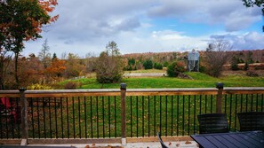 A wooden deck with a metal railing, overlooking a grassy area with trees and a silo in the distance. - Rural spacious farmhouse w/ hot tub and can sleep 10, located 15m from Truro (Greenfield)