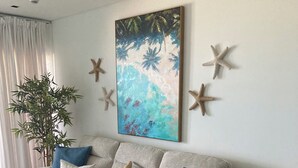 En stue med en beige sofa, blå og hvide puder, en stjerneskive som pynt, et maleri af en strandscene og en potteplante.
