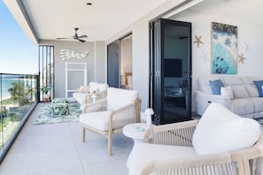 A balcony with wicker furniture, a view of the ocean, and a painting of sea life on the wall.