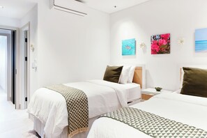 A hotel room with two beds, a small bedside table, a nightstand, and a wall with three framed artworks.