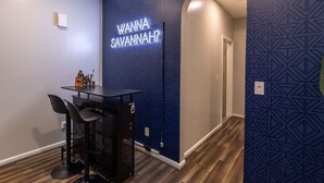 Une pièce avec un panneau néon sur lequel on peut lire « ENVIE D’ALLER À SAVANNAH ? » et un coin bar avec des tabourets et une petite table.
