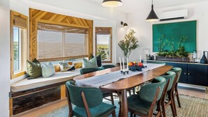 Un comedor con una mesa de madera, sillas tapizadas de verde y un banco con cojines.