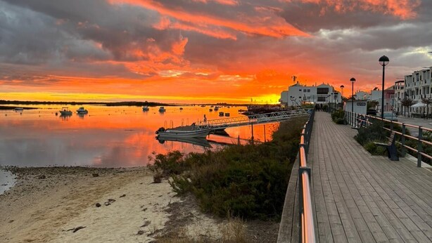 Une promenade en bois longeant une plage, avec un coucher de soleil en arrière-plan.