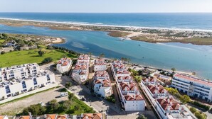 Une zone résidentielle côtière avec des bâtiments blancs et des toits recouverts de tuiles rouges, un port de plaisance et une plage en arrière-plan.