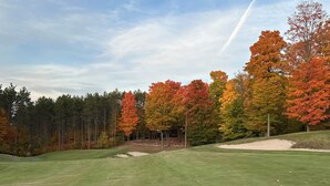 Un parcours de golf bordé d’arbres aux couleurs automnales, sous un ciel dégagé, avec un gazon bien entretenu.