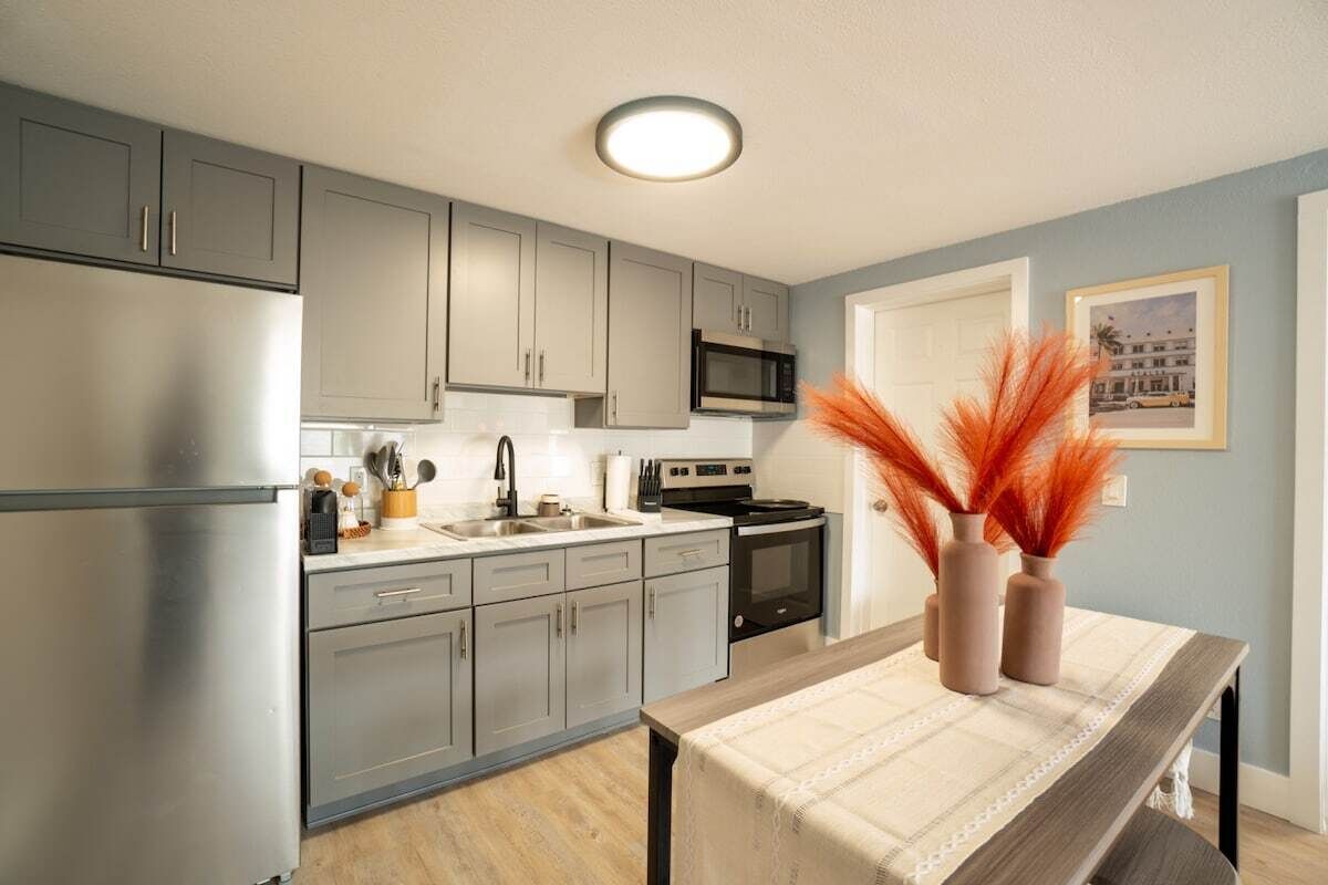 Una cocina moderna con gabinetes grises, electrodomésticos de acero inoxidable y una zona de comedor con una mesa preparada para dos.