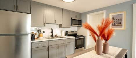 A modern kitchen with grey cabinets, stainless steel appliances, and a dining area with a table set for two.