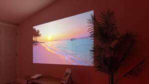 Une pièce dans laquelle est installé un projecteur mural diffusant une scène de coucher de soleil, une petite table avec un livre et une plante en pot.