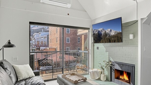A modern living room with a leather sofa, a fireplace, and a balcony with a city view. - Slope-Side| Modern Remodel | Hot Tub | Park Free (Park City)