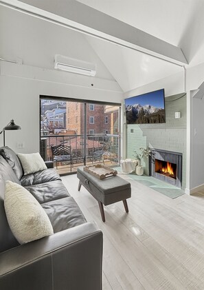 A modern living room with a leather sofa, a fireplace, and a balcony with a city view. - Slope-Side| Modern Remodel | Hot Tub | Park Free (Park City)