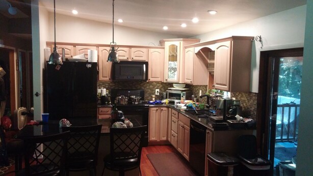 A kitchen with wooden cabinets, a black refrigerator, a microwave, and a sink. There are chairs and a dining table.