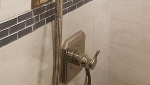 A shower with a chrome finish, a handheld showerhead, and a wall-mounted control panel.