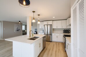A modern kitchen with white cabinetry, stainless steel appliances, and pendant lighting.