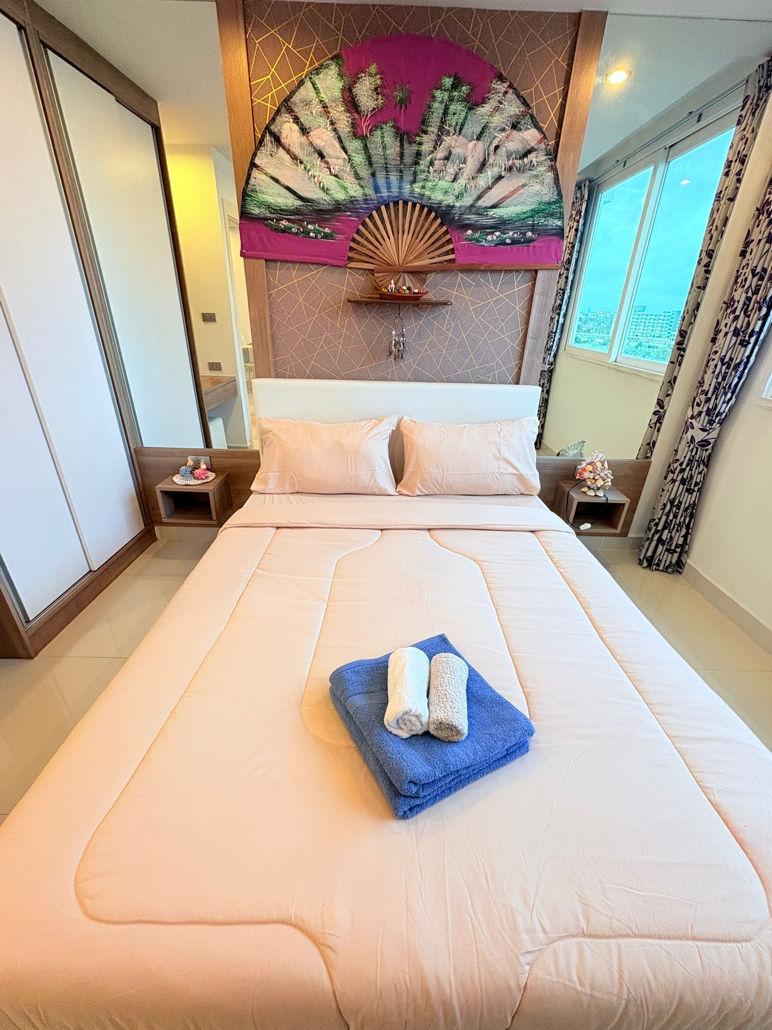 Habitación de hotel con una cama grande, un tapiz decorativo y vistas a la ciudad a través de la ventana.