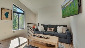 Un salon moderne avec un canapé gris, une table basse en bois et un grand téléviseur fixé au mur.