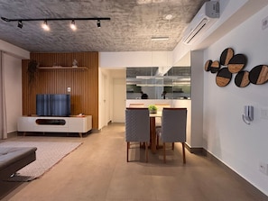 A modern living room with a TV, seating, and a dining area with a table and chairs. - ID Vida Urbana (Goiânia)