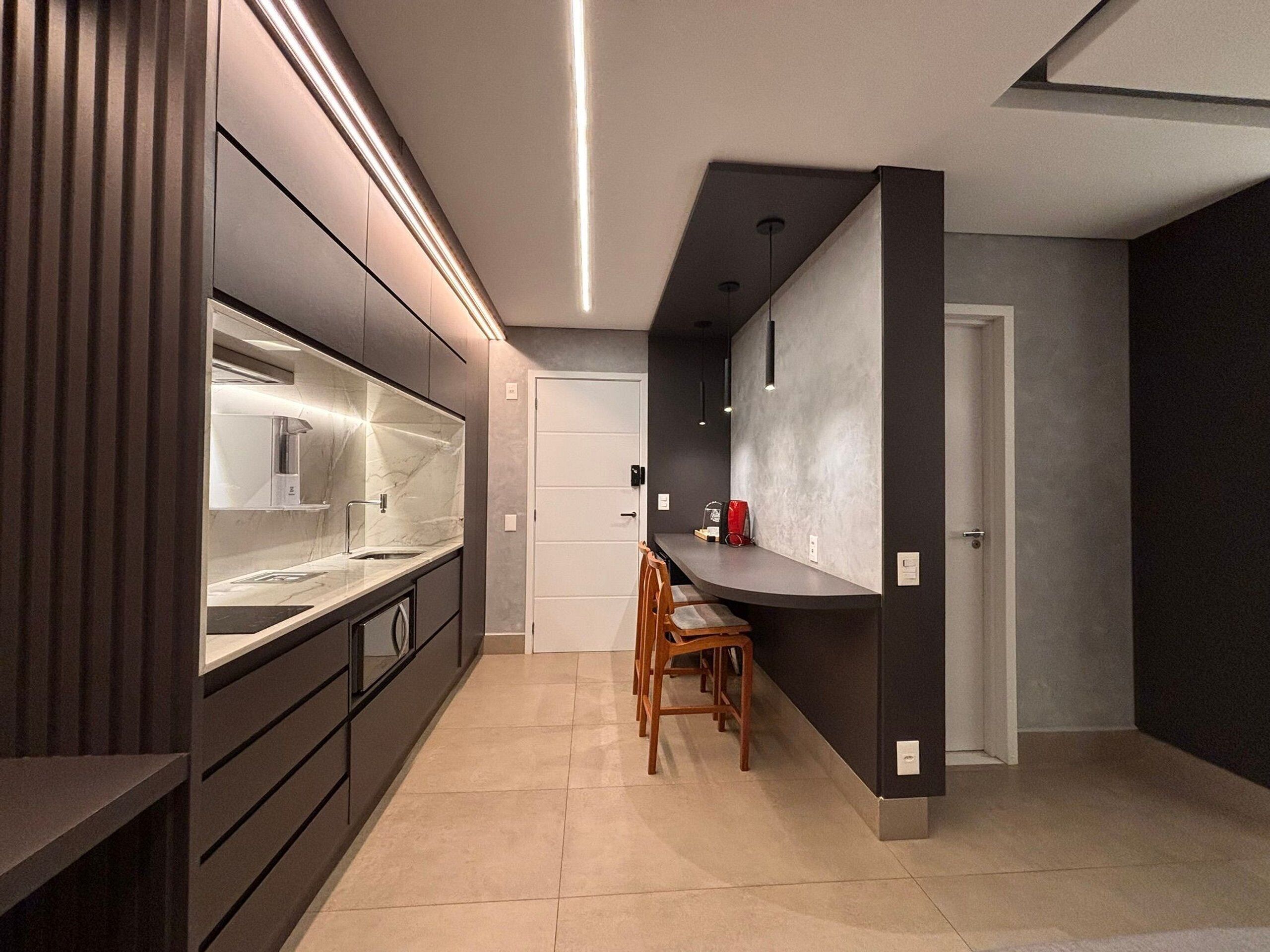 Una cocina moderna con horno empotrado, lavamanos y zona de comedor con sillas.