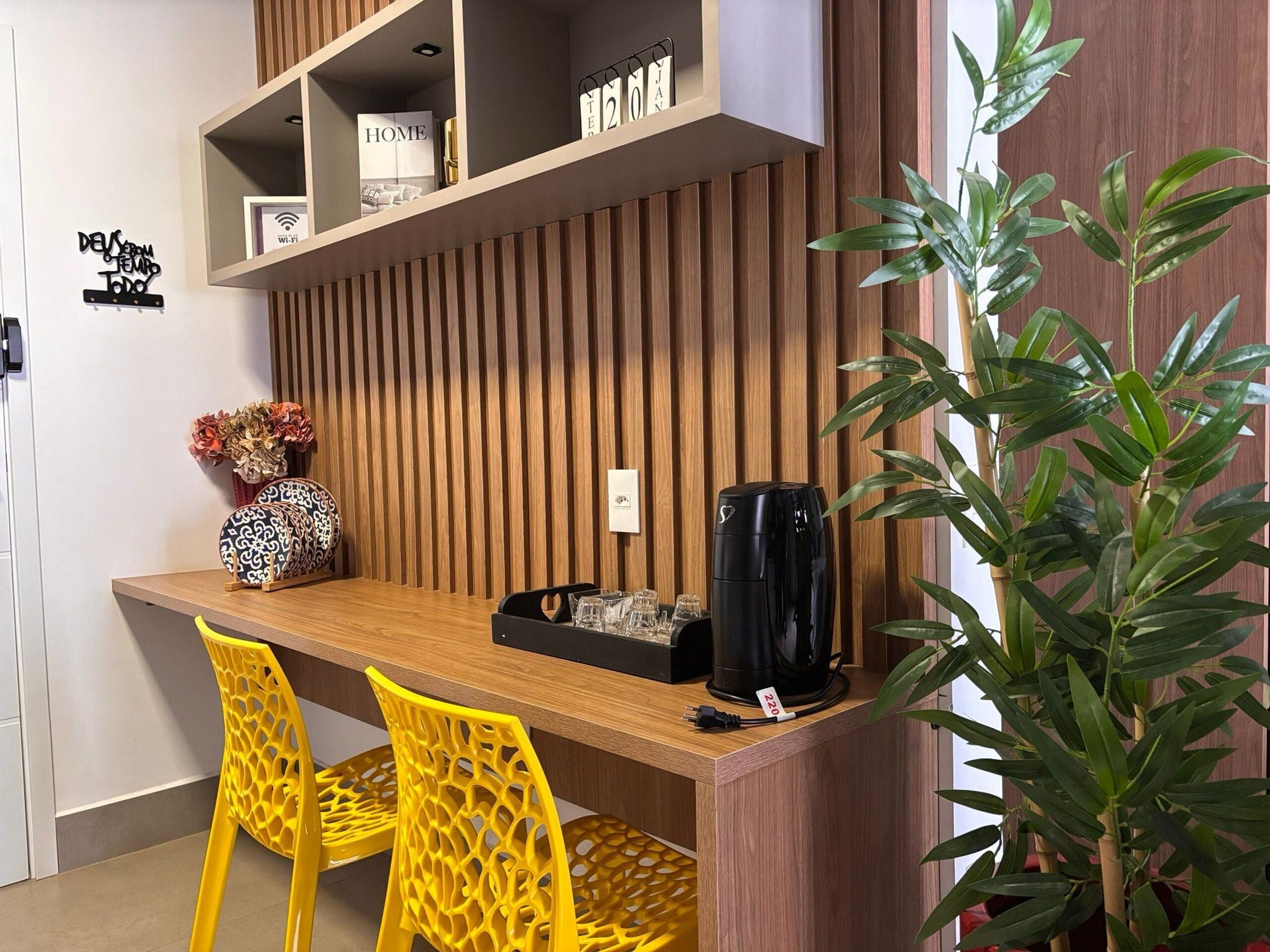 A modern kitchen with a wooden countertop, two yellow chairs, a black coffee maker, and a potted plant.
