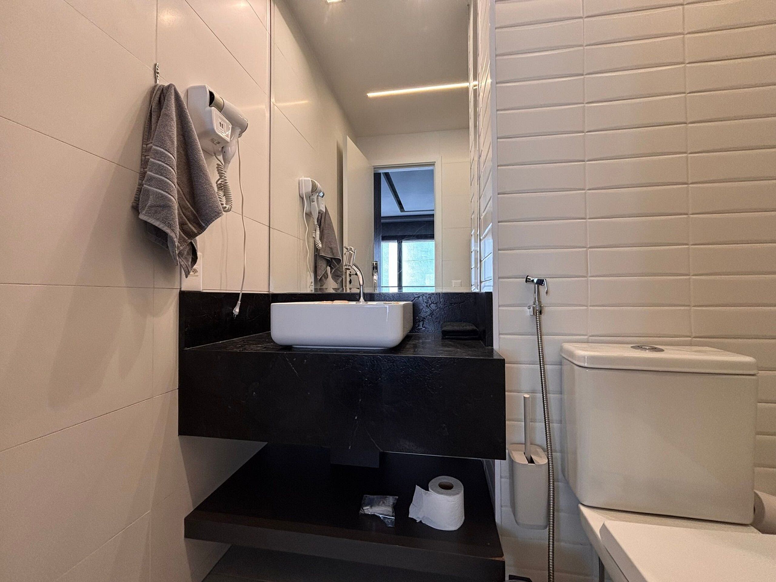 A modern bathroom with a white sink, black countertop, and a toilet.