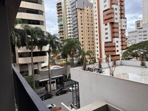 A high-rise building with multiple balconies, a swimming pool, and surrounding palm trees. - ID Vida Urbana (Goiânia)