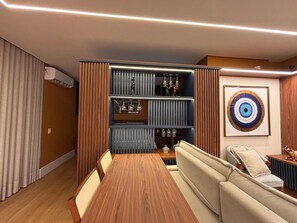 A modern living room with a wooden dining table, a sofa, and a built-in shelving unit with decorative items. - ID Vida Urbana (Goiânia)