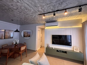 A living room with a TV, dining table, chairs, and artwork on the walls. - ID Vida Urbana (Goiânia)