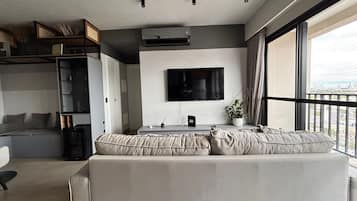 A modern living room with a sofa, a TV, and a balcony view.