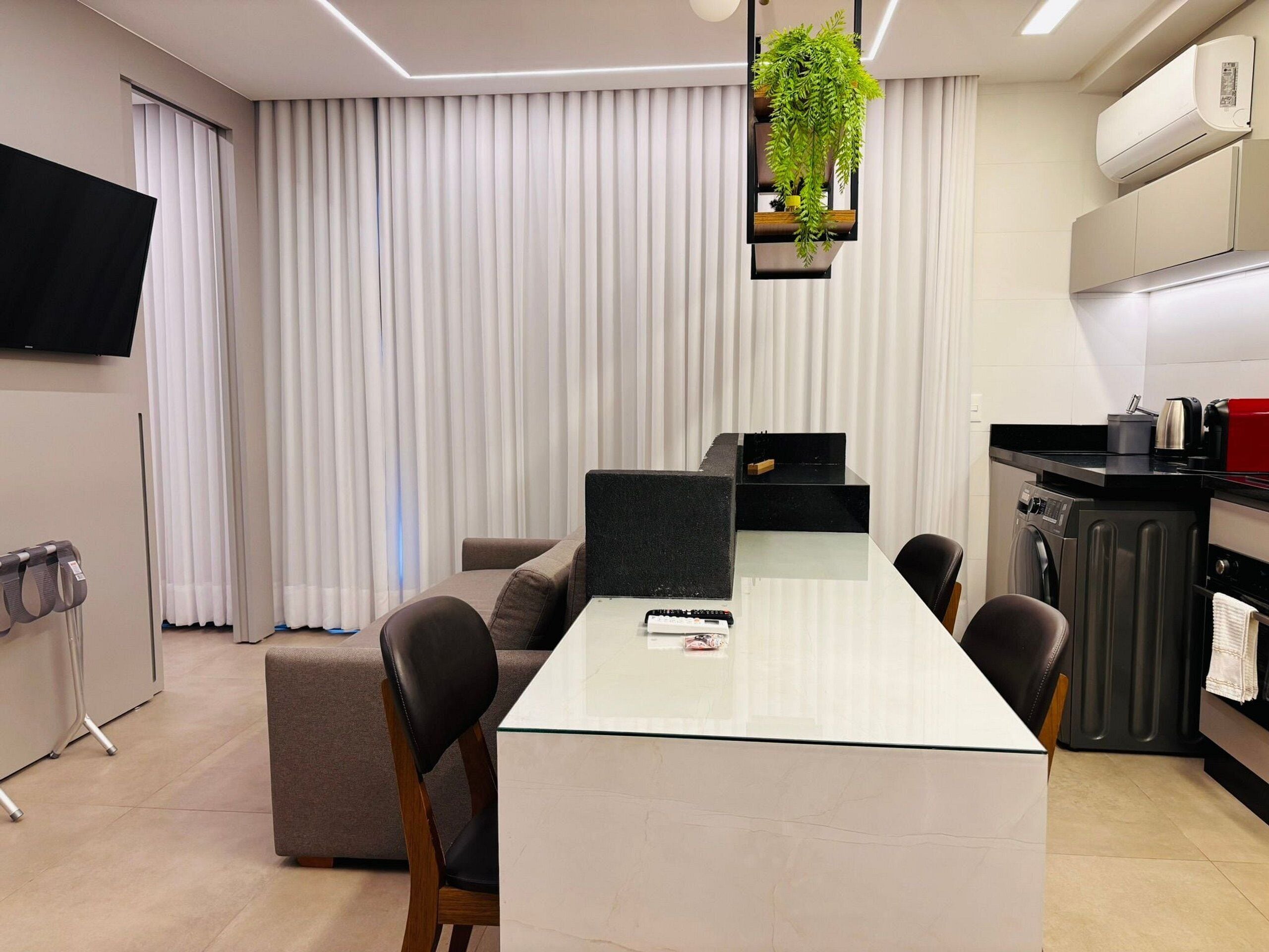 Una cocina moderna con una isla central, un comedor con mesa de vidrio y un espacio de sala de estar con sofá.