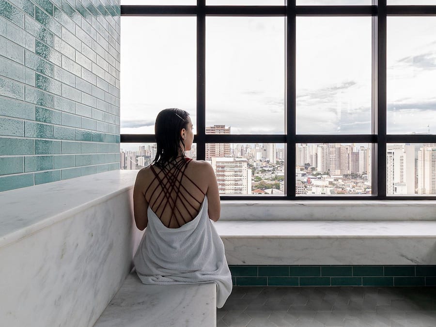 A person sitting on a bench by a large window with a city view.