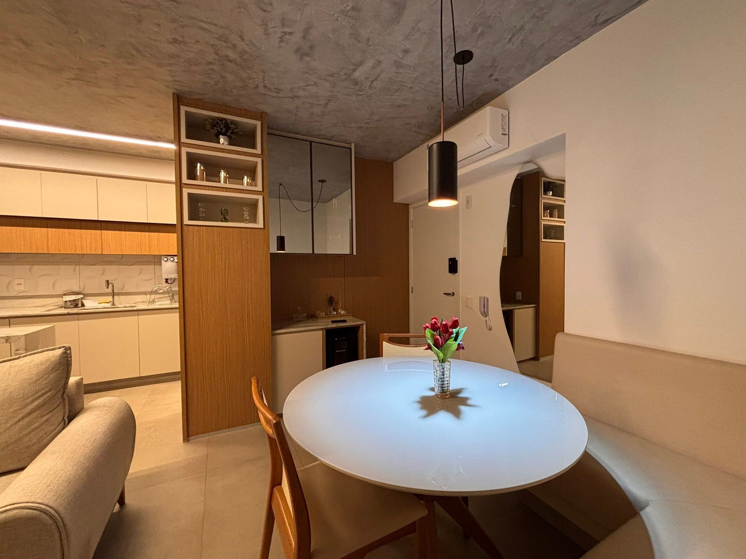 Cozinha moderna com armários de madeira, uma mesa de jantar branca com um vaso de flores e um forno embutido.