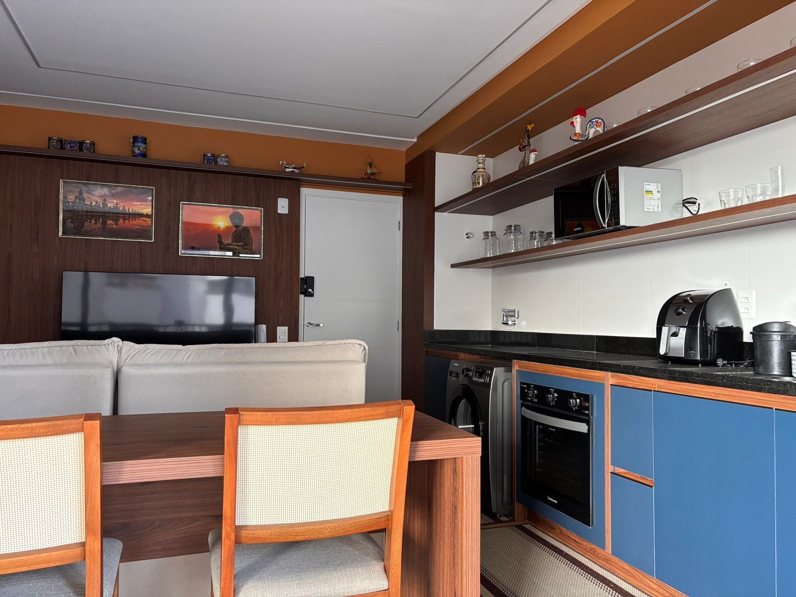 A compact kitchen with a microwave, toaster, and coffee maker, a dining area with a sofa and chairs, and a TV.