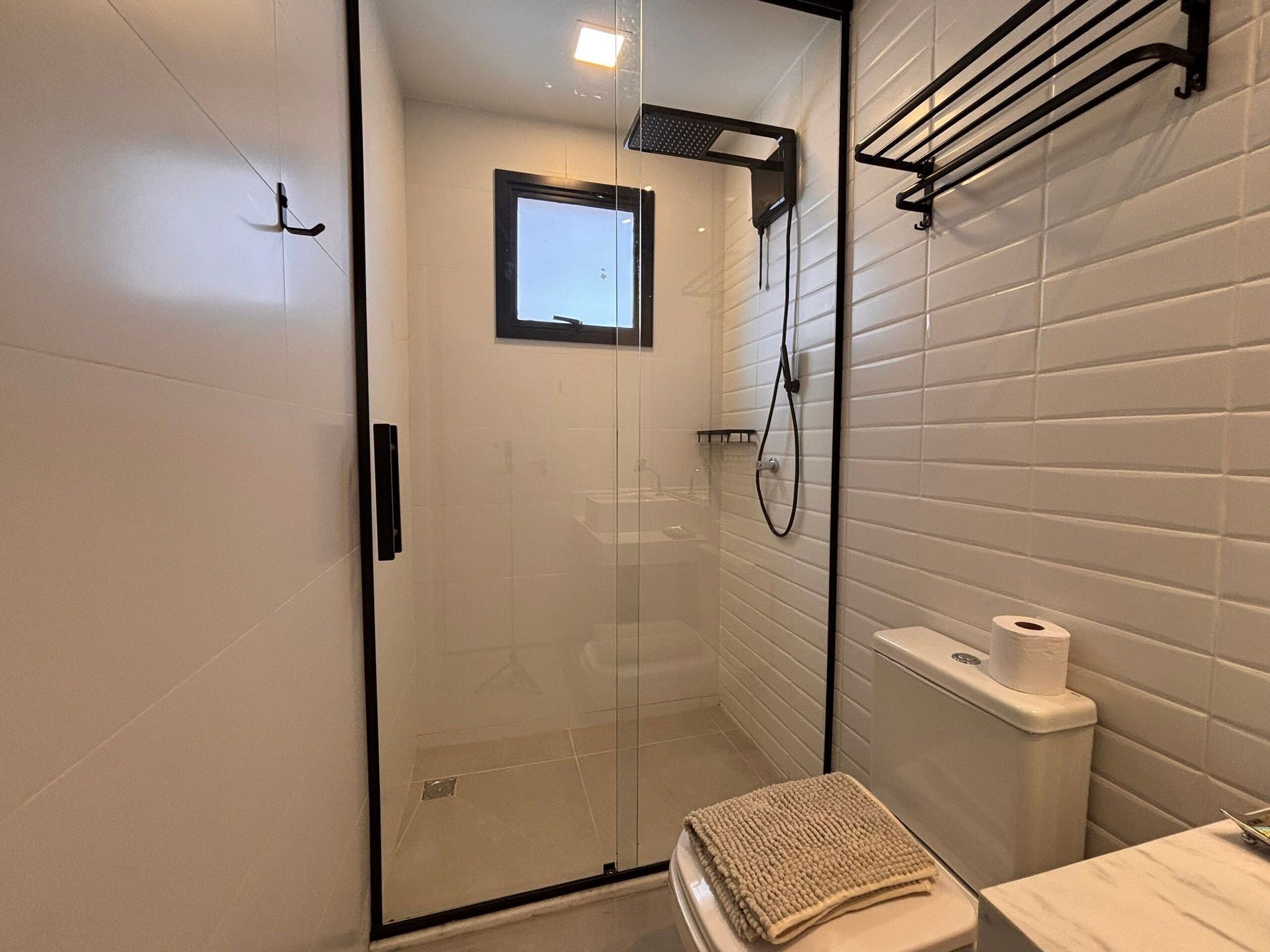 A modern bathroom with a glass-enclosed shower, a toilet with a towel, and a shelf with toiletries.