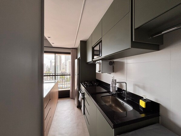 A modern kitchen with a large window, a stainless steel sink, and a black countertop. - ID Vida Urbana (Goiânia)