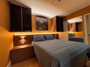 A bedroom with a bed, nightstands, a wall-mounted TV, a framed picture, and a mirror. - ID Vida Urbana (Goiânia)