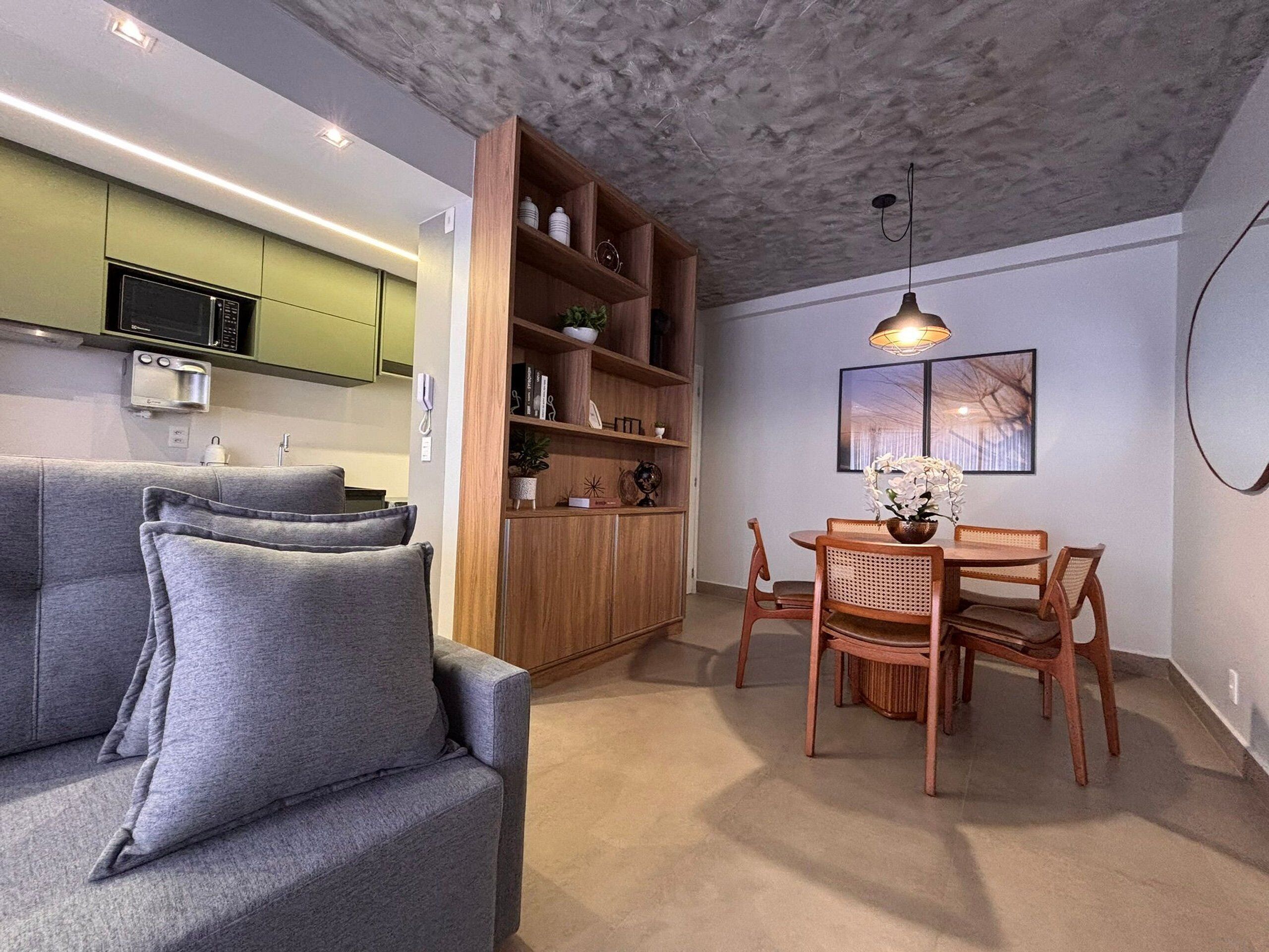 Een moderne leefruimte met een bank, eettafel, stoelen, een houten boekenkast en een keuken.