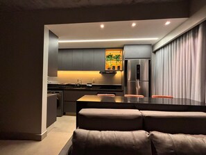 A modern kitchen with a central island, built-in appliances, and a seating area with a sofa. - ID Vida Urbana (Goiânia)