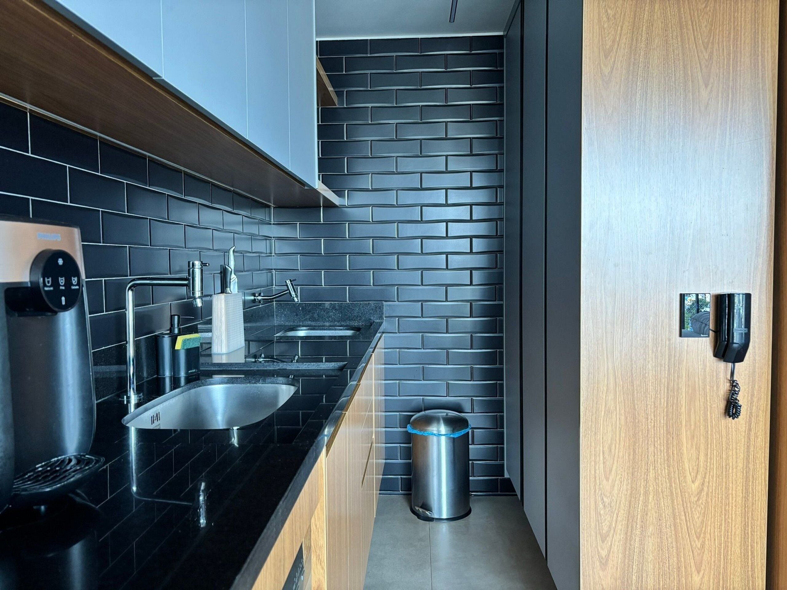 A modern kitchen with black countertops, stainless steel appliances, and a black brick backsplash.