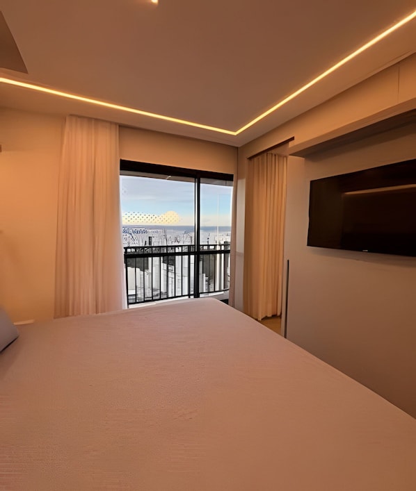 A hotel room with a large bed, a TV mounted on the wall, and a balcony with a city view. - ID Vida Urbana (Goiânia)