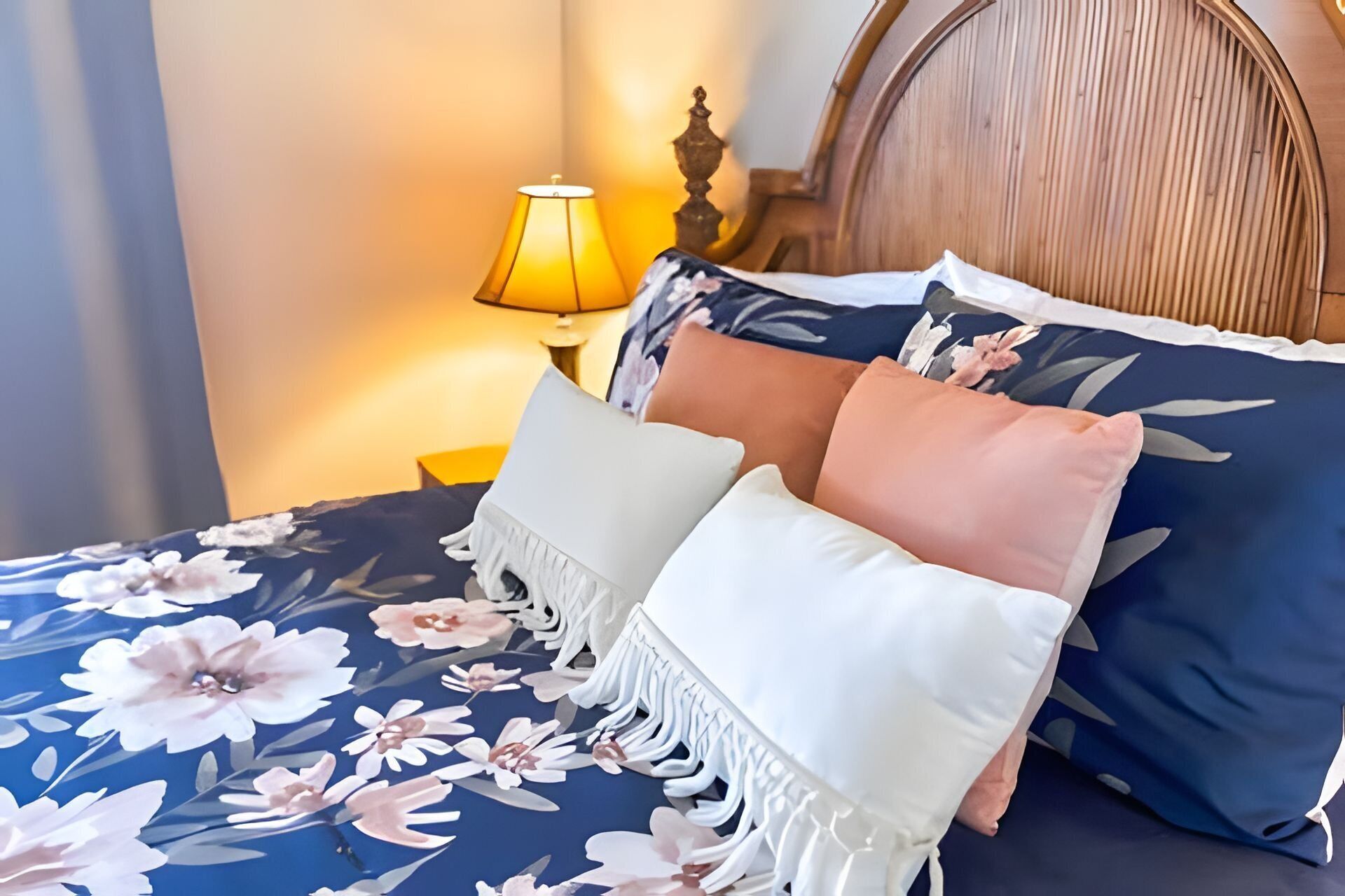 Ein Bett mit blumigem Bettzeug, mehreren Kissen und einem hölzernen Kopfteil.
