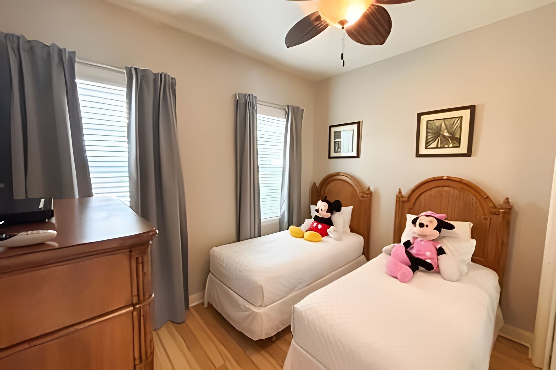A hotel room with two beds, a ceiling fan, a TV, and a desk.