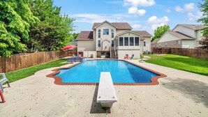 Un jardin avec une piscine, une terrasse en bois et une maison dotée d’un porche à l’avant.
