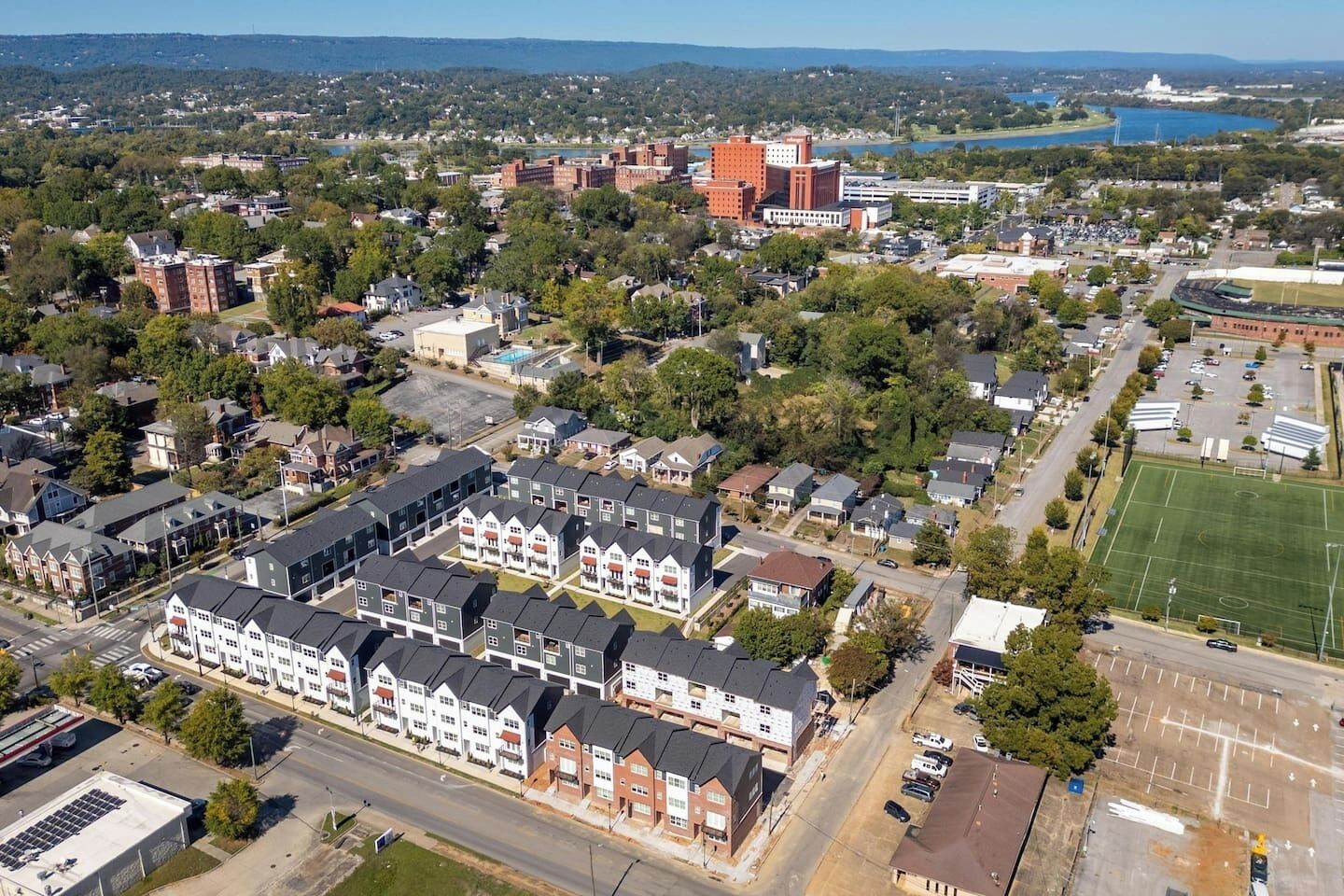 An aerial view of a residential area with houses, a large building with a red roof, and a sports field.