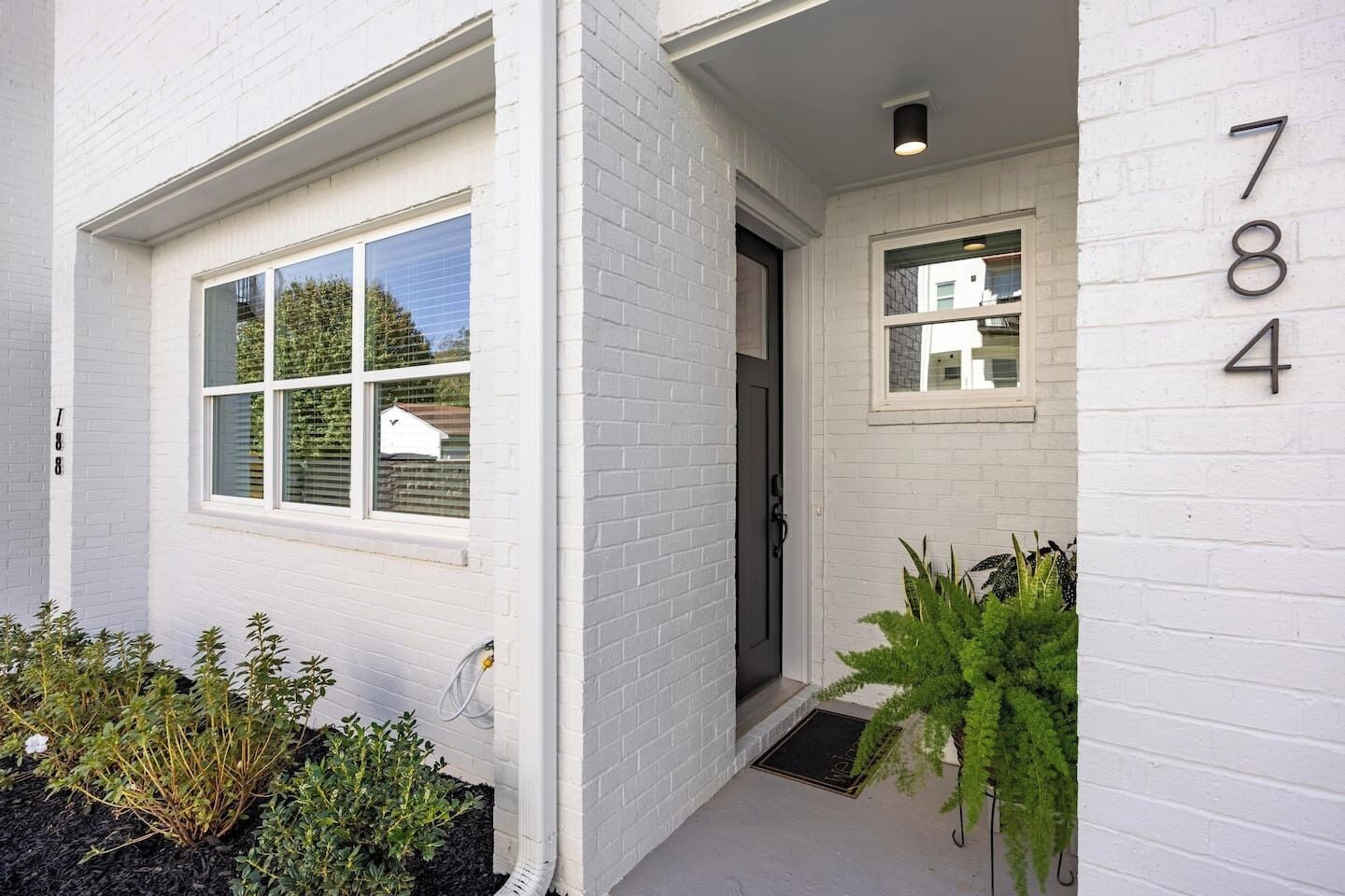Een wit huis van baksteen met een voordeur, een klein portiek en een raam met het nummer 784 op de gevel.